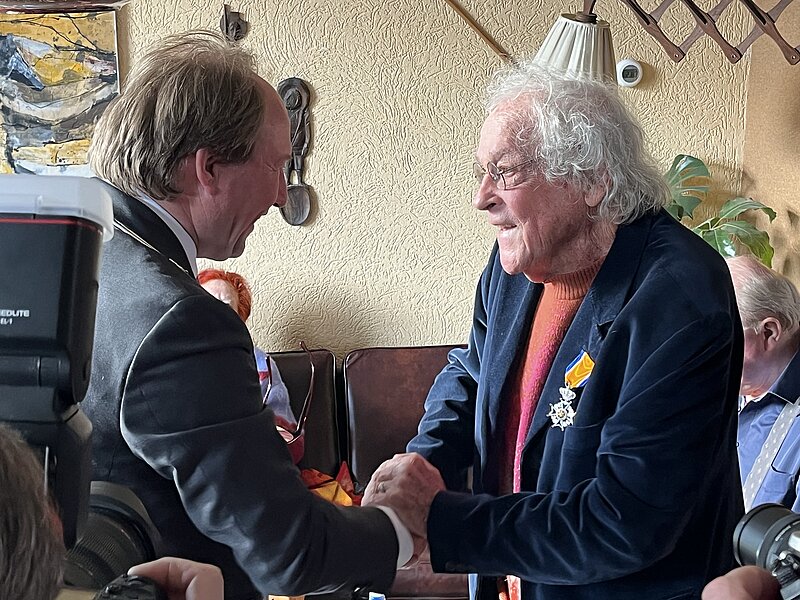 kleurenfoto van moment dat Hans Laumanns lintje krijgt van burgemeester Hein van der Loo op 10 april 2026, foto Stadsarchief Almere