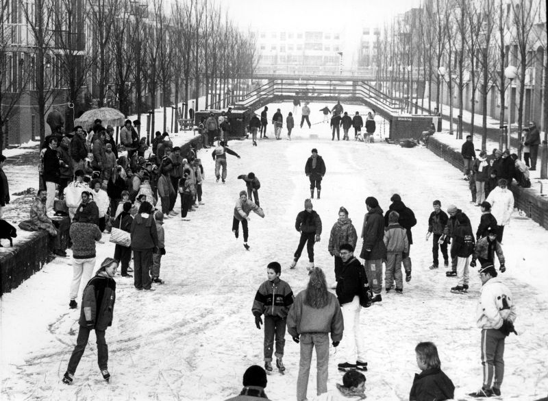 Zwart-wit foto van Bob Friedländer uit de collectie van Stadsarchief Almere van schaatsende mensen op de Olstgracht in Almere Stad